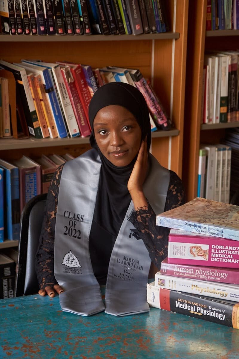 Young female graduate in a library with books, Zaria, Nigeria.